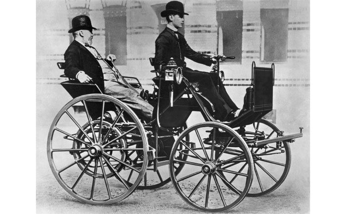 Gottlieb Daimler in seiner Motorkutsche von 1886, dem ersten vierrädrigen Benzinautomobil der Welt. Am Steuer Daimlers Sohn Adolf (1871-1913).